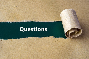 Torn brown paper on green surface with "Questions" word.