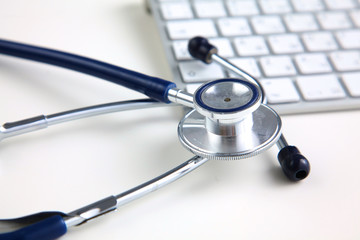 A medical stethoscope near a laptop on a wooden table, on white