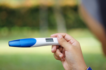 Holding digital pregnancy test with bokeh background. The pregna