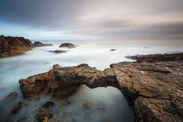 Maravilhosa praia de Cascais com a sua ponde de pedra. Paisagem da costa Portuguesa, perto de Lisboa. Fotografia horizontal com efeito de longa exposição.