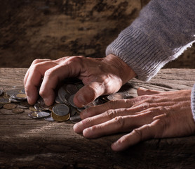Close up of  caucasian old man's hands  and pile of old coins on a wooden background