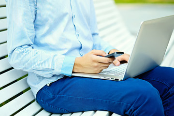 Young man working with laptop, man's hands on notebook computer, business person in casual clothes in the street