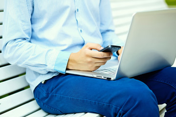Young man working with laptop, man's hands on notebook computer, business person in casual clothes in the street