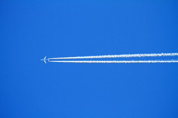 Airplane with condensation trails on blue sky.