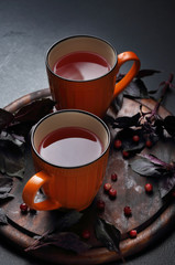 Cranberry tea in orange cup on wooden board decorated with basil leafs and berry.