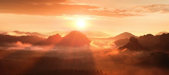 Red misty daybreak in a beautiful hills. Peaks of hills are sticking out from foggy background,  red and orange  fog below Sun rays.
