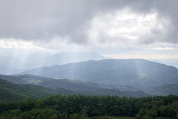 The sun rays pierce through the cloudy sky on to the ancient landscape of the Blue Ridge Mountains looking from the Appalachian Trail in North Carolina
