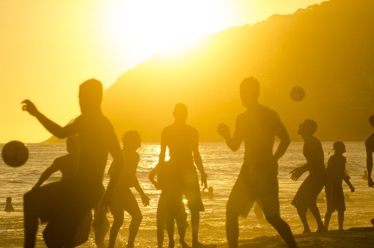 Golden sunset silhouettes of Brazilians playing keepy uppy altinho beach football soccer at Posto Nove, on Ipanema Beach, Rio de Janeiro, Brazil