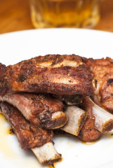 Roasted pork ribs on a white plate with a pitcher of beer next