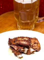 Roasted pork ribs on a white plate with a pitcher of beer next