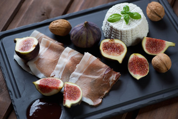 Basalt plate with ricotta, ham, fresh figs and walnuts, close-up