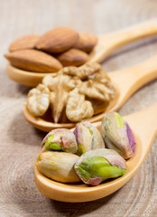 Almonds, walnuts and pistachio on a wooden spoon.