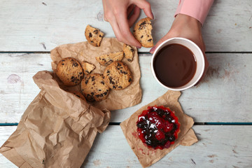 Female hands holding cup of coffee and cookies on wooden table close up
