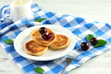 Fritters of cottage cheese with cherry and cream in plate on checkered napkin, closeup