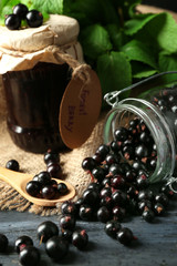 Ripe blackcurrant in glass jar and tasty jam on wooden background