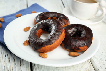 Delicious doughnuts with chocolate icing and cup of coffee on table close up
