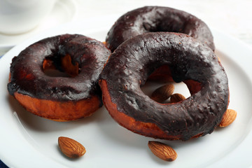 Delicious doughnuts with chocolate icing and nuts on plate close up