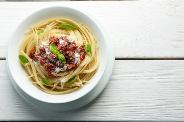 Spaghetti Bolognese with parmesan cheese in white bowl, on color wooden background