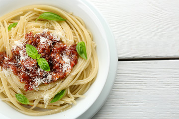 Spaghetti Bolognese with parmesan cheese in white bowl, on color wooden background
