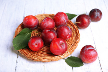 Ripe plums in wicker tray on wooden background