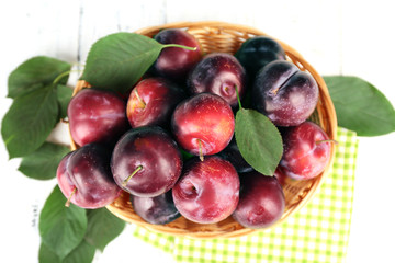 Ripe plums in wicker bowl on wooden table with napkin, closeup