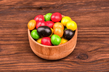 A bowl full of colored candy on a wooden brown background