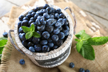 Tasty ripe blueberries with green leaves in bucket on table close up