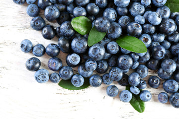 Tasty ripe blueberries with green leaves on wooden table close up