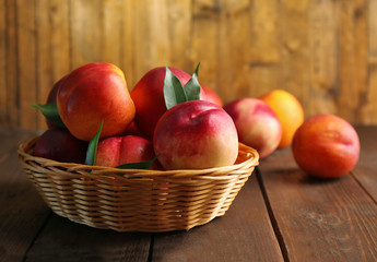Fresh peaches in wicker basket on wooden background