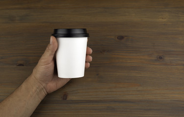 Paper cup of coffee in hand on wooden background