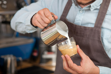 Cheerful young barista is brewing coffee in cafe
