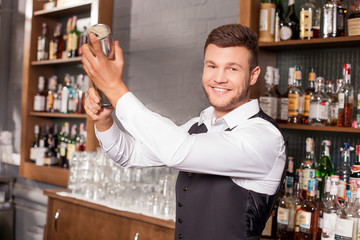 Attractive young male bartender is shaking cocktail