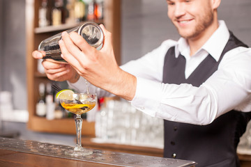 Attractive young male barman is preparing alcohol drink