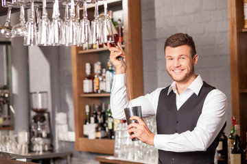 Cheerful male barman is mixing beverage in bar