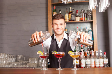 Cheerful male barman is mixing beverage in bar