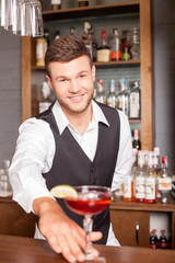Handsome male bartender is giving drink to customer
