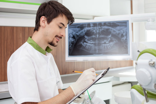 Attractive male dentist is analyzing teeth in office