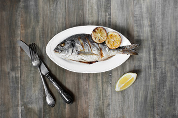 Prepared fish on the white plate, on the old wooden table