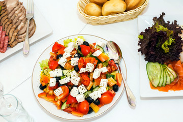 Salad with vegetables and feta, salad peppers, tomatoes and cheese, a dish with salad, white tablecloth with a table setting, healthy food, diet food, Breakfast, lunch, and dinner. Healthy eating.