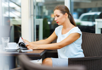 Attractive woman with red lips reads a newspaper sitting in a ca