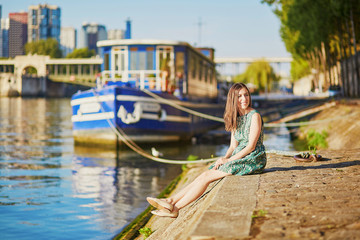 Happy young girl sitting on the bank of the Seine