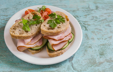 sandwich with whole grain bread, cucumber and ham on a white plate on blue wooden surface