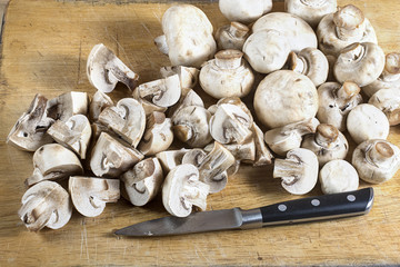 Fresh whole and cutted champignons on a cutting board with a kni