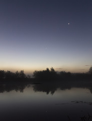 Obraz premium Riverside just before sunrise. Trees reflected in the water. Stars in the sky.