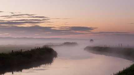 Fototapeta na wymiar River in the fog, just before sunrise. Warm glow in the clouds from the first sunrays.