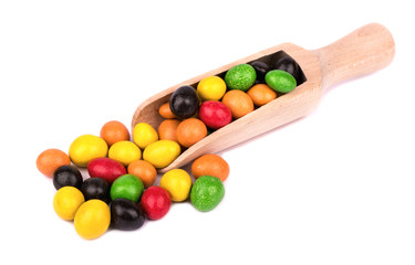 A pile of multi-colored candies in chocolate peanuts in a wooden scoop on a white background