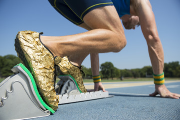 Athlete in gold shoes starting a race from the starting blocks on a blue running track 