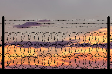 Silhouette of a metal fence with barbed wire
