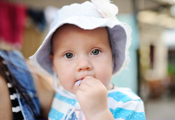 baby girl at mum on hands sucks her finger and looking at the ca