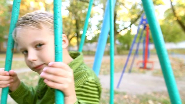 Cute child on swing. Little boy rides on swing on children playground. Slow motion portrait of funny face of little 8 years old kid playing outside on autumn warm sunny day.